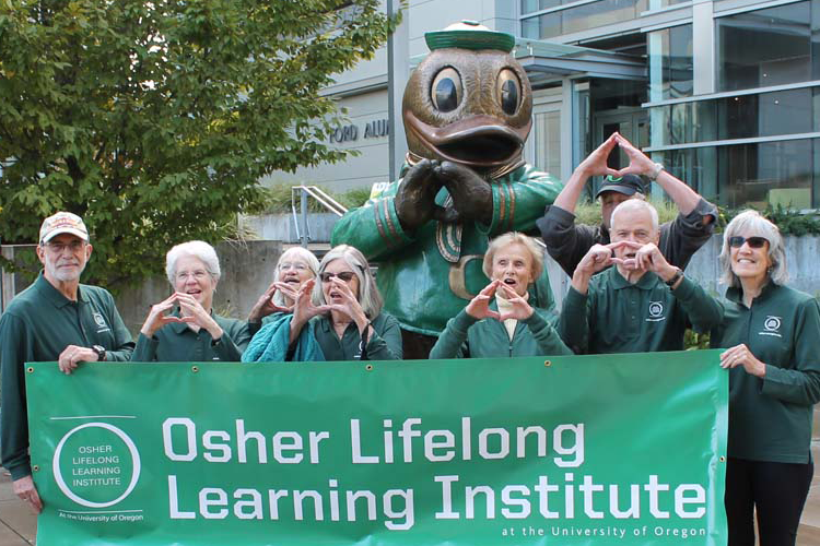 Photo of eleven adults in University of Oregon clothing holding a banner that reads Osher Lifelong Learning Institute in front of UO campus building.