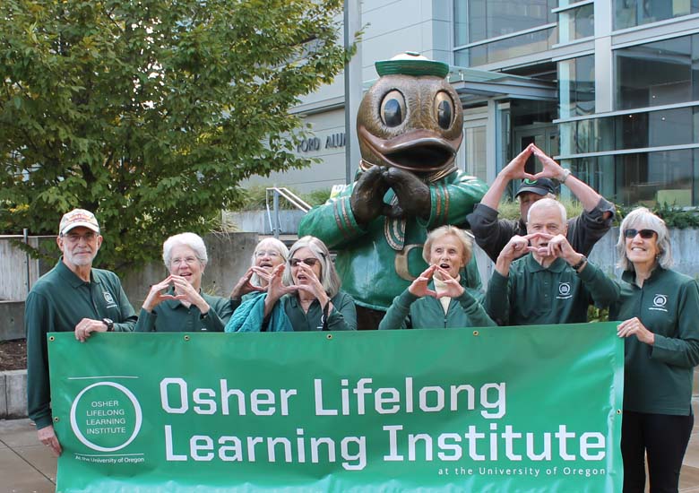 Photo of eleven adults in University of Oregon clothing holding a banner that reads Osher Lifelong Learning Institute in front of UO campus building.