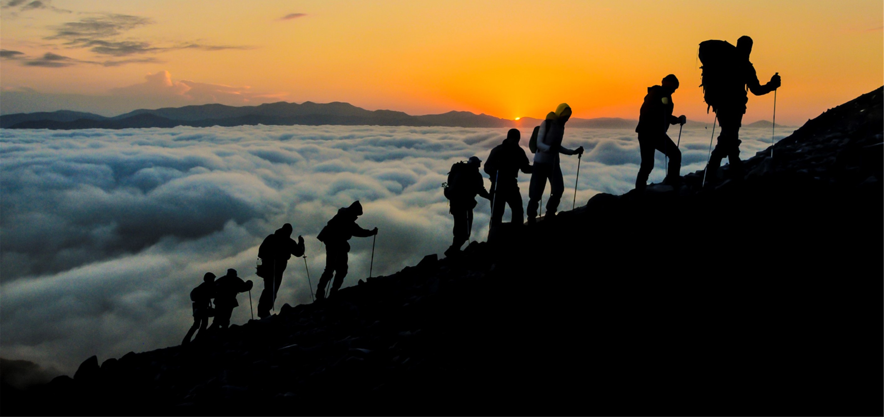 Backpackers climbing a mountain at sunset.